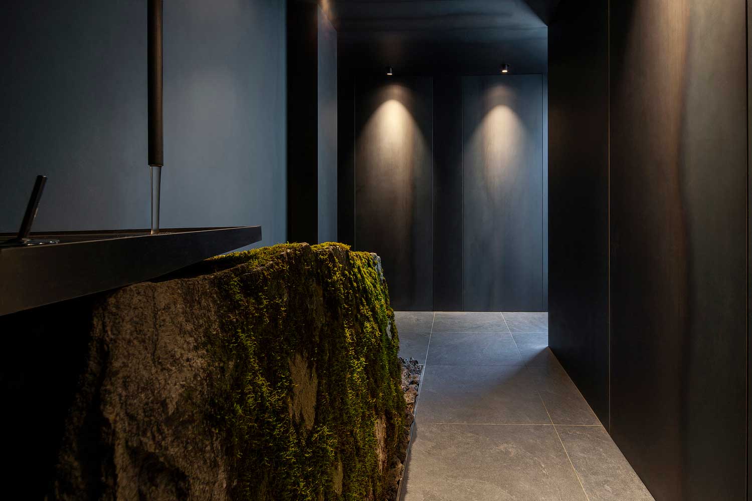 The bathroom features a sink that rests atop a moss-covered boulder